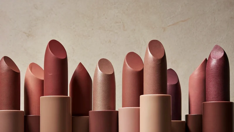 Matte Lippenstifte in Rosé-, Nude- und Beerentönen aufrecht auf hellem Putz, illustrativ.