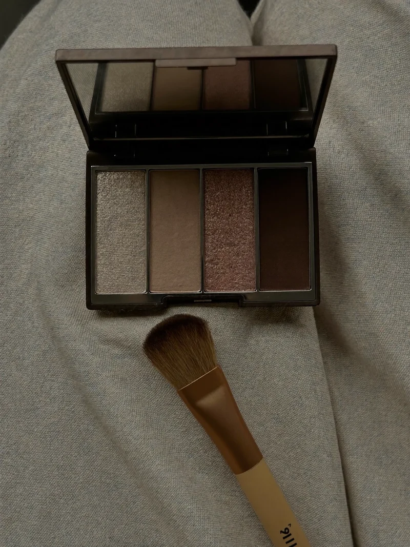 Geöffnete Lidschatten-Palette mit weichem Blendingpinsel auf Leinen, Aufsicht, illustrativ.
